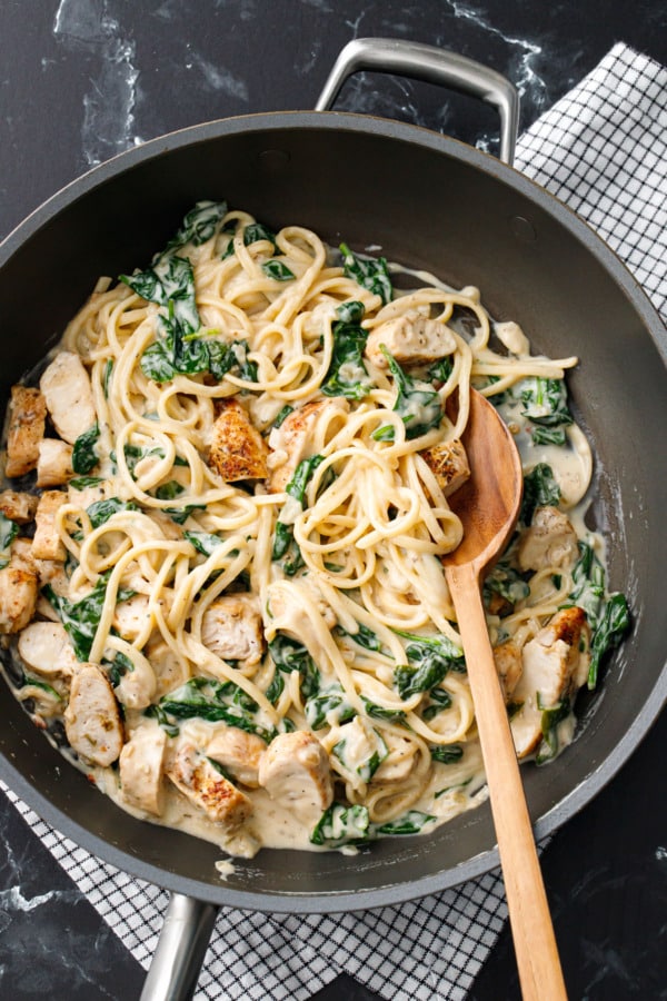 Creamy Chicken Florentine Pasta in a nonstick skillet, stirred together with visible bits of spinach and pan-seared chicken tenders.
