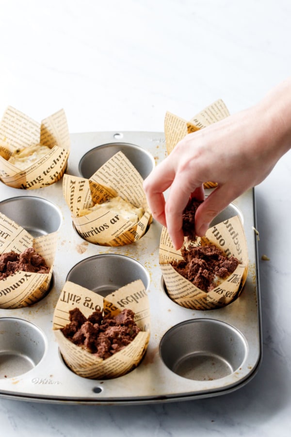 Sprinkling chocolate streusel on top of orange chocolate chunk muffins, in a silver muffin tin lined with paper tulip wrappers.