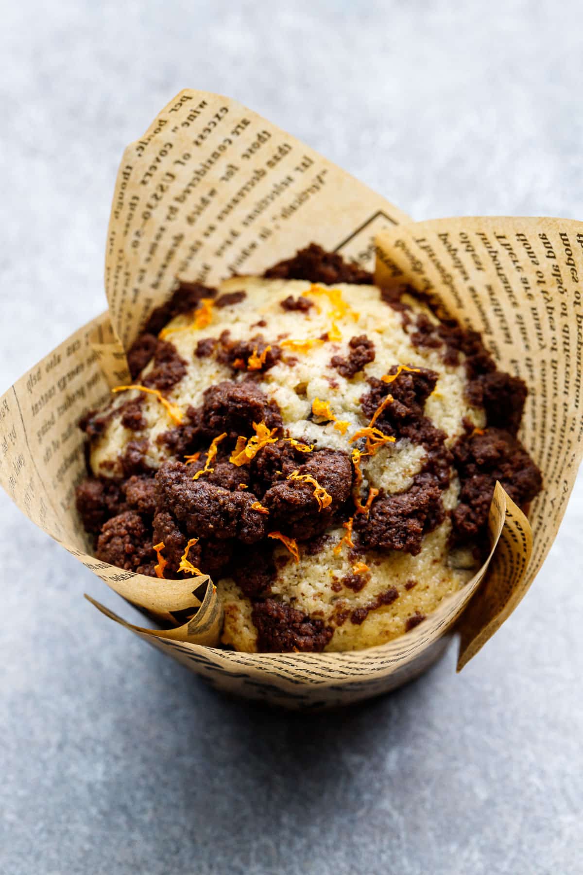 Closeup, Chocolate Orange Muffin topped with a chocolate streusel and finely grated orange zest, in a newsprint tulip paper wrapper.