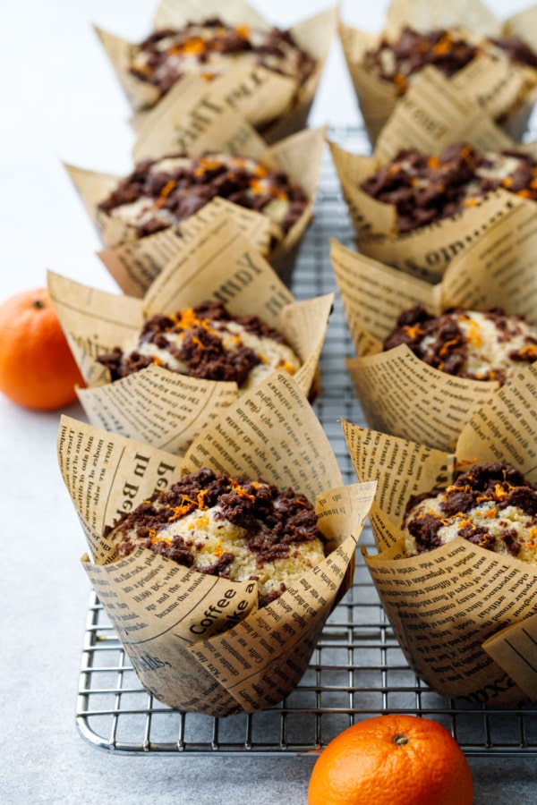 Rows of Chocolate Orange Streusel Muffins on a wire baking rack, with two mandarin oranges on the side for flavor reference.