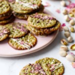 Pistachio Florentine Cookies on a pink plate with scattered pistachios and rose petals around.