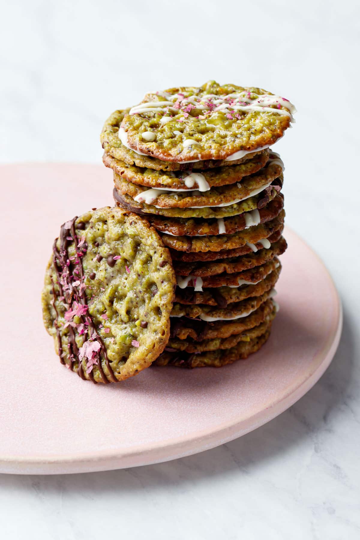 Tall off kilter stack of Pistachio Florentine Cookies on a pink plate, one cookie leaning against the side to show the decoration on top.