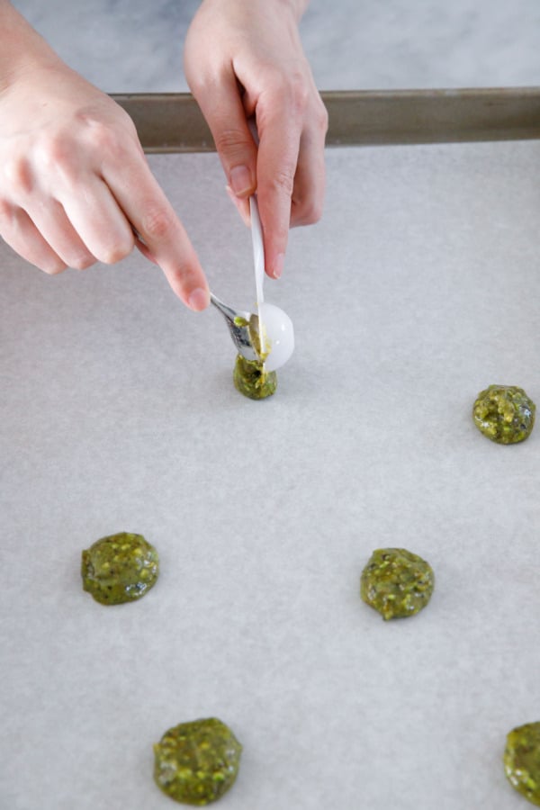 Dropping teaspoonfuls of Pistachio Florentine Cookie batter onto a partchment-lined baking sheet.