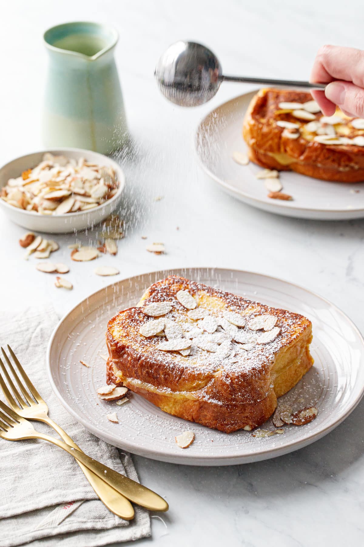 Marzipan-Stuffed French Toast on a plate, action shot dusting the top with powdered sugar.