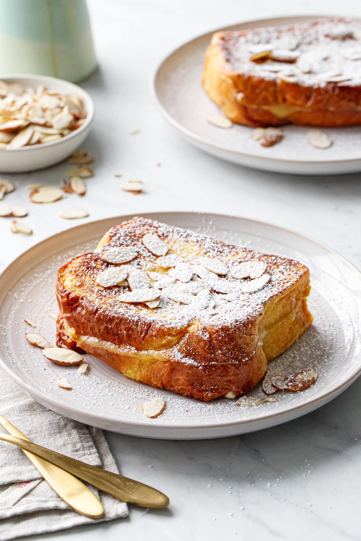Two plates with Marzipan-Stuffed French Toast, topped with almonds and dusted with powdered sugar.