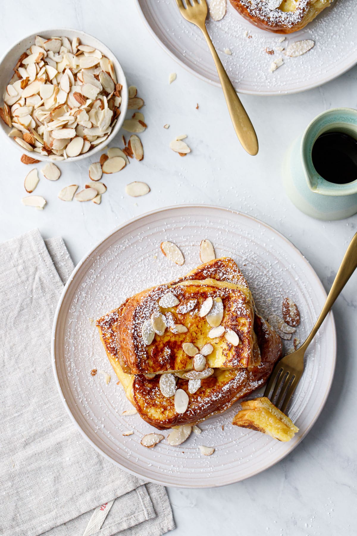 Overhead, plates with Marzipan-Stuffed French Toast and a bowl of almonds and pitcher of maple syrup.