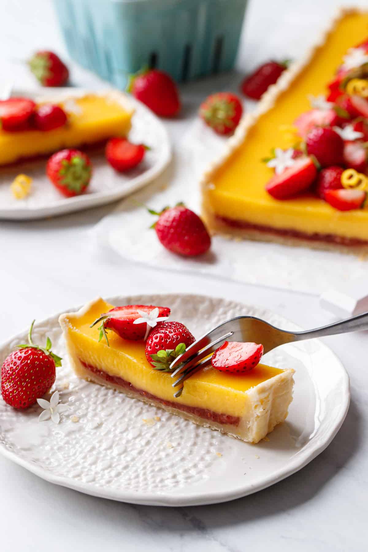 Fork cutting into a slice of Strawberry Meyer Lemon Tart, showing the soft texture of the meyer lemon curd and layer of strawberry jam underneath.