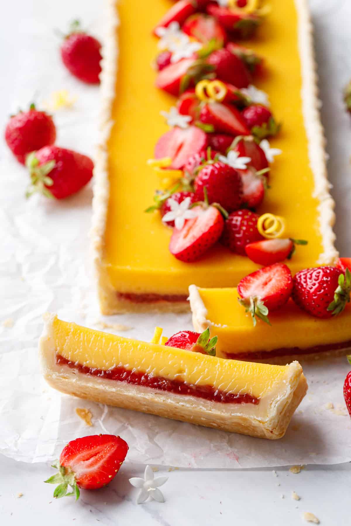Strawberry Meyer Lemon Tart with bright yellow lemon curd filling and a layer of strawberry jam on the bottom.