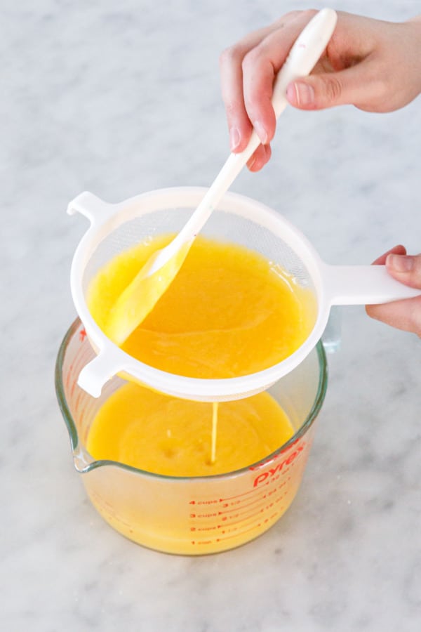 Straining lemon curd through a nylon mesh strainer.