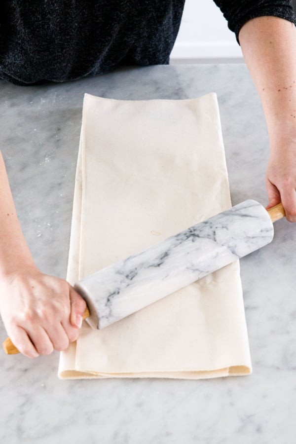 Rolling pie dough folded inside a pastry cloth to form a rectangular shape.