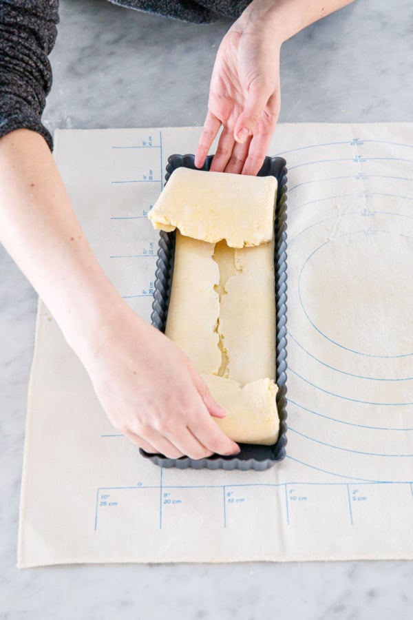 Folded dough being lowered gently into the rectangular tart pan.