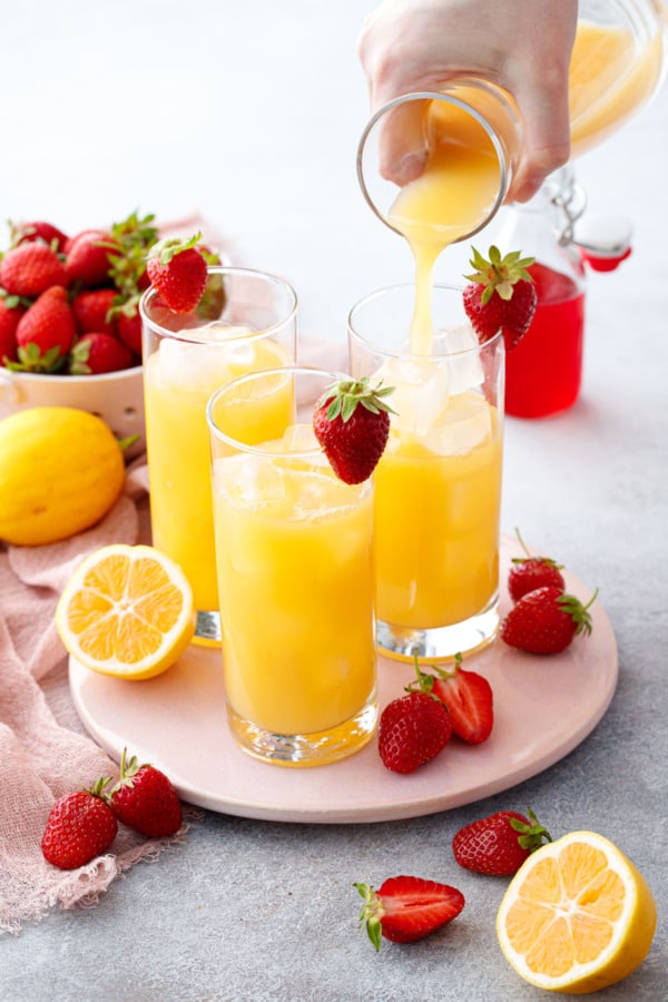 Pouring bright yellow passionfruit lemon mixture into three ice-filled glasses.