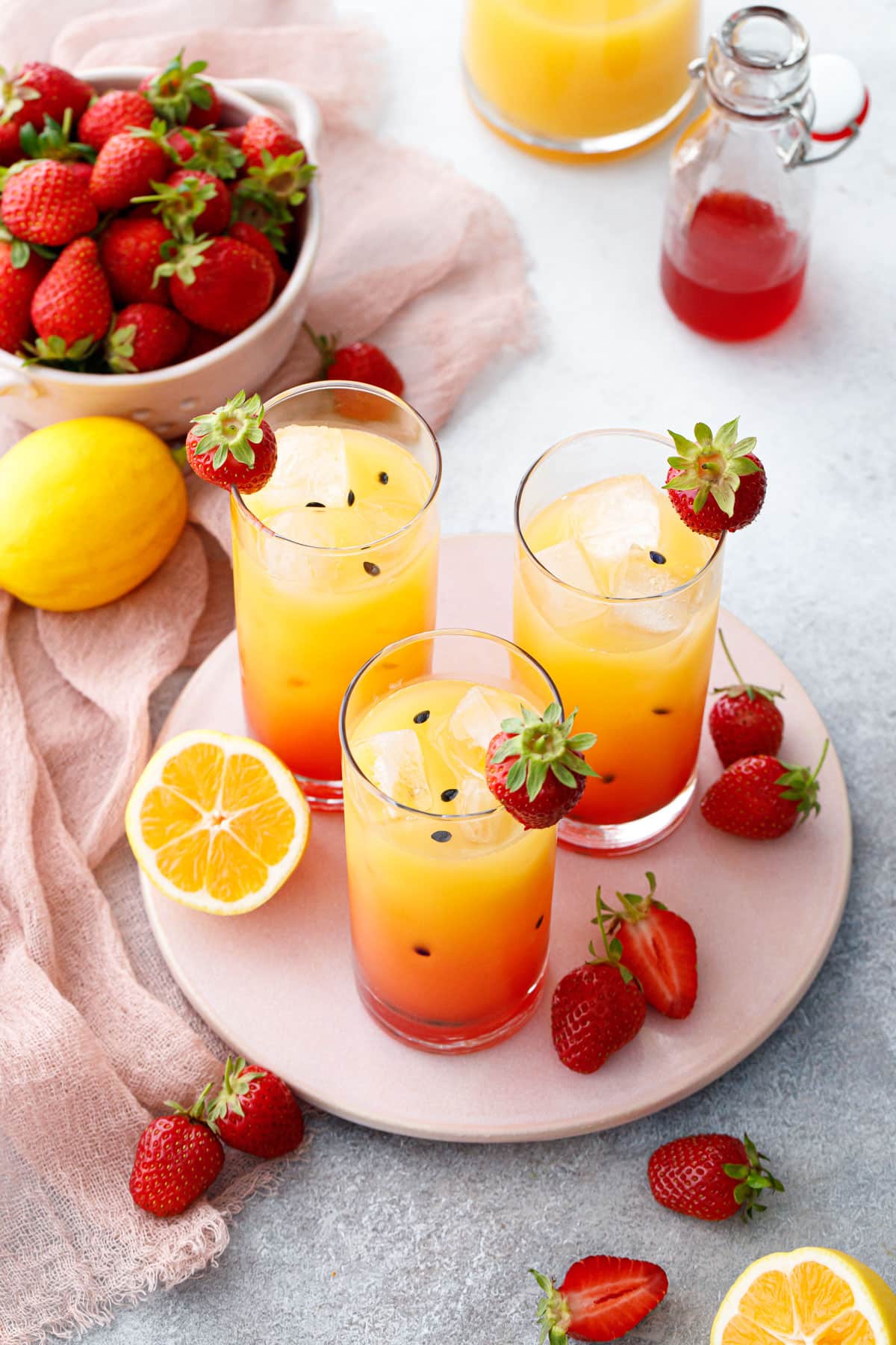 Три стакана клубничного лимонада с маракуйей, окрашенного градиентом от красного к желтому с черными семенами маракуйи.