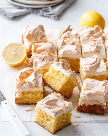 Cut squares of Lemon Meringue Butter Cake on a marble background with white knife and stack of plates in the background.