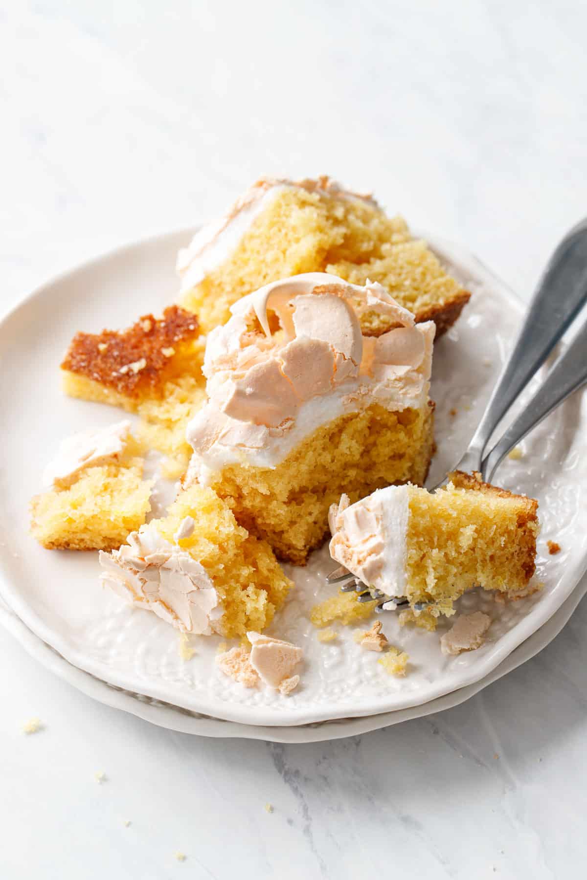 Messy plate with crumbly pieces of Lemon Meringue Butter Cake and a fork on a marble background.