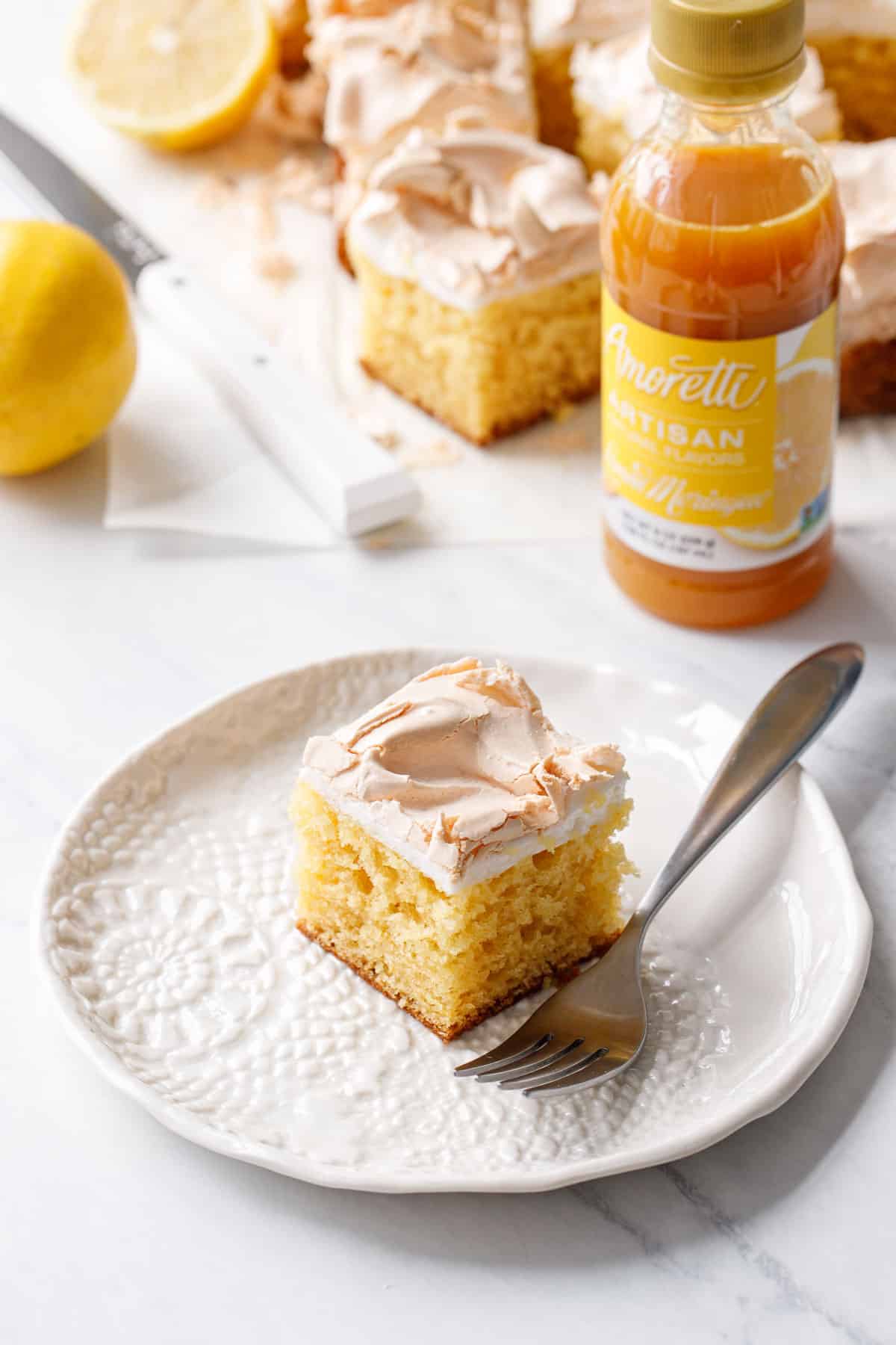 Piece of Lemon Meringue Butter Cake on a plate with a fork, bottle of lemon meringue flavoring in the background.
