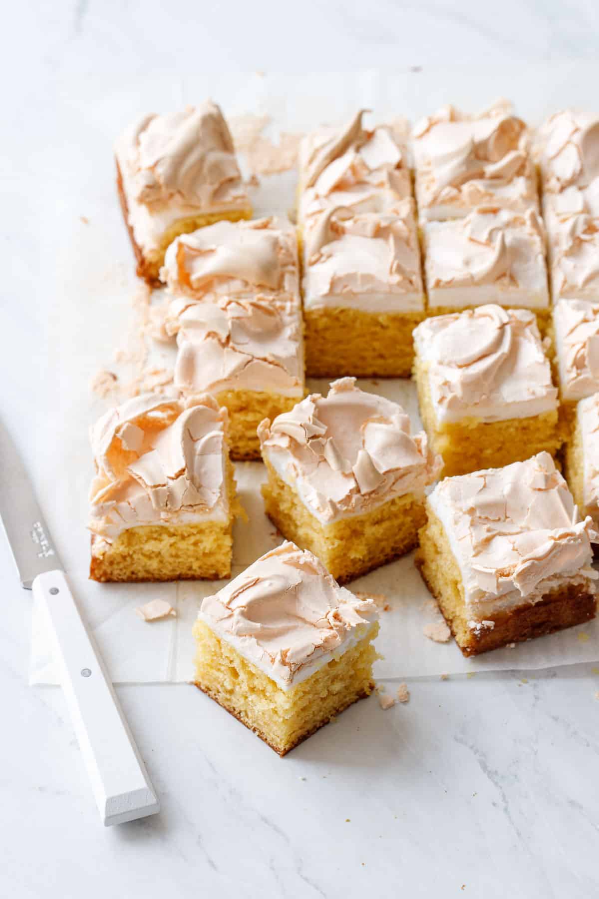 Lemon Meringue Butter Cake cut into squares, arranged on a piece of parchment paper with a small white knife.