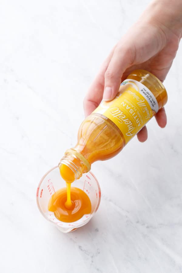 Pouring Amoretti's Lemon Meringue Artisan Flavoring into a small measuring beaker, showing the thick consistency and bright yellow color.