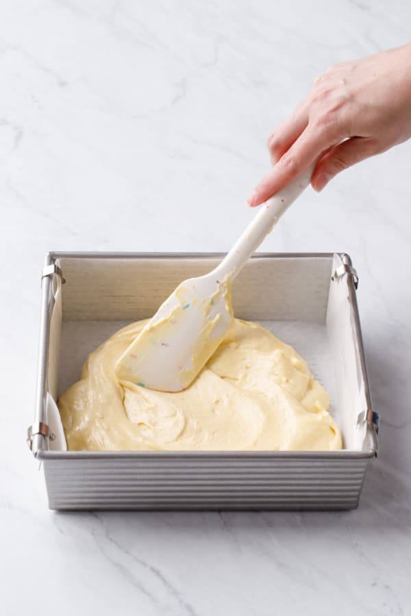 Spreading the thick lemon butter cake batter into the baking pan with a spatula.