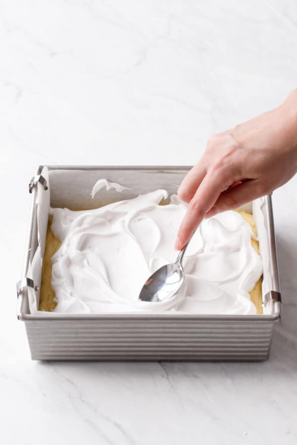 Using a spoon to swoop and swirl the meringue on top of the cake.