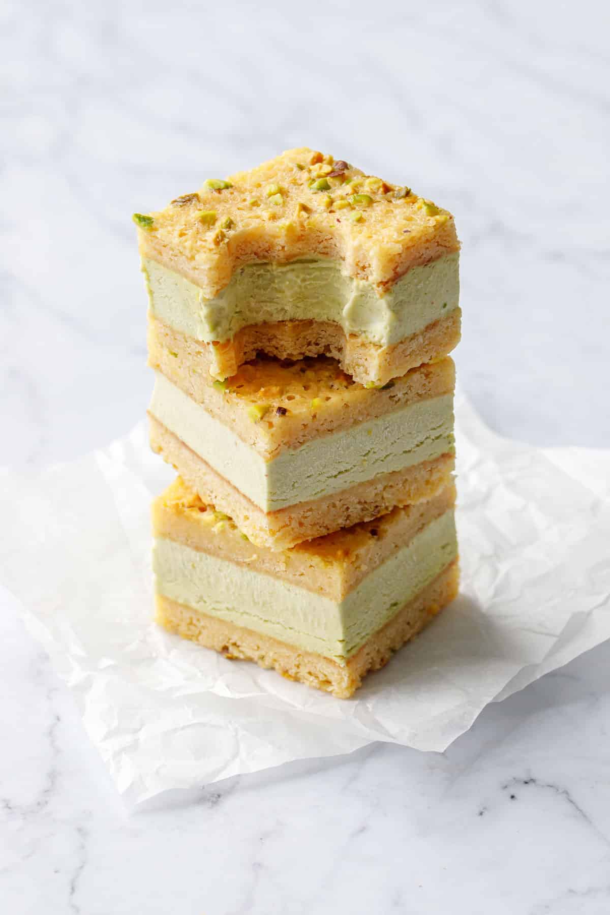 Stack of square cut Pistachio Blondie Ice Cream Sandwiches, one with a bite cut out of it to show the texture and layers.