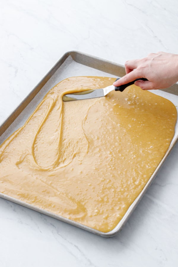 Using an offset spatula to spread the blondie batter in an even layer in the half-sheet pan.