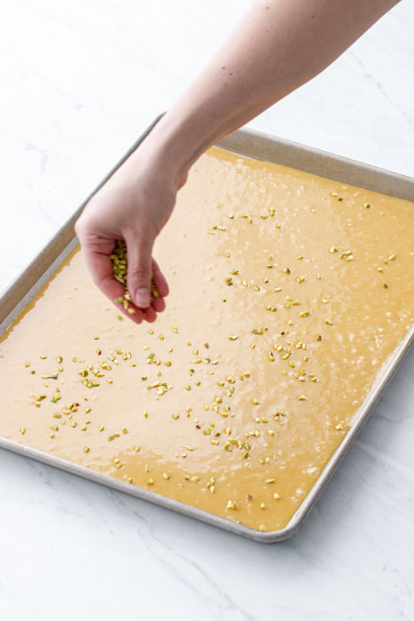Sprinkling the unbaked blondie batter with chopped pistachios before baking.