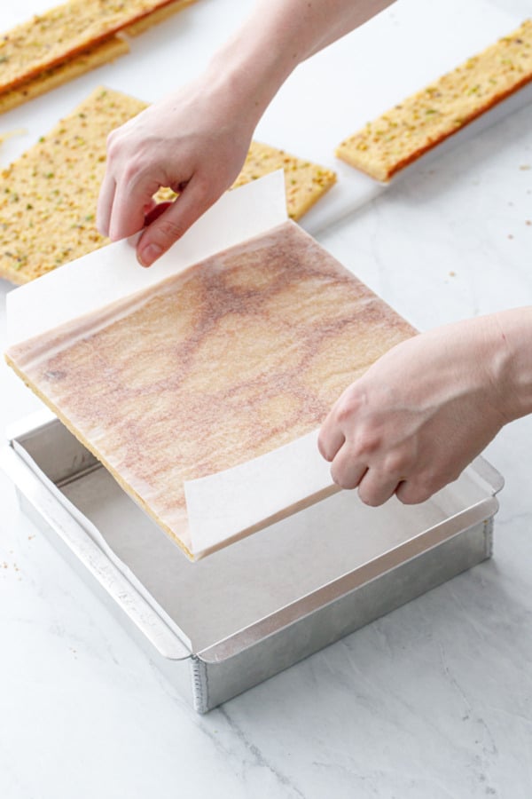 Lowering one of the blondie squares into a parchment-lined 8-by-8-inch baking pan.