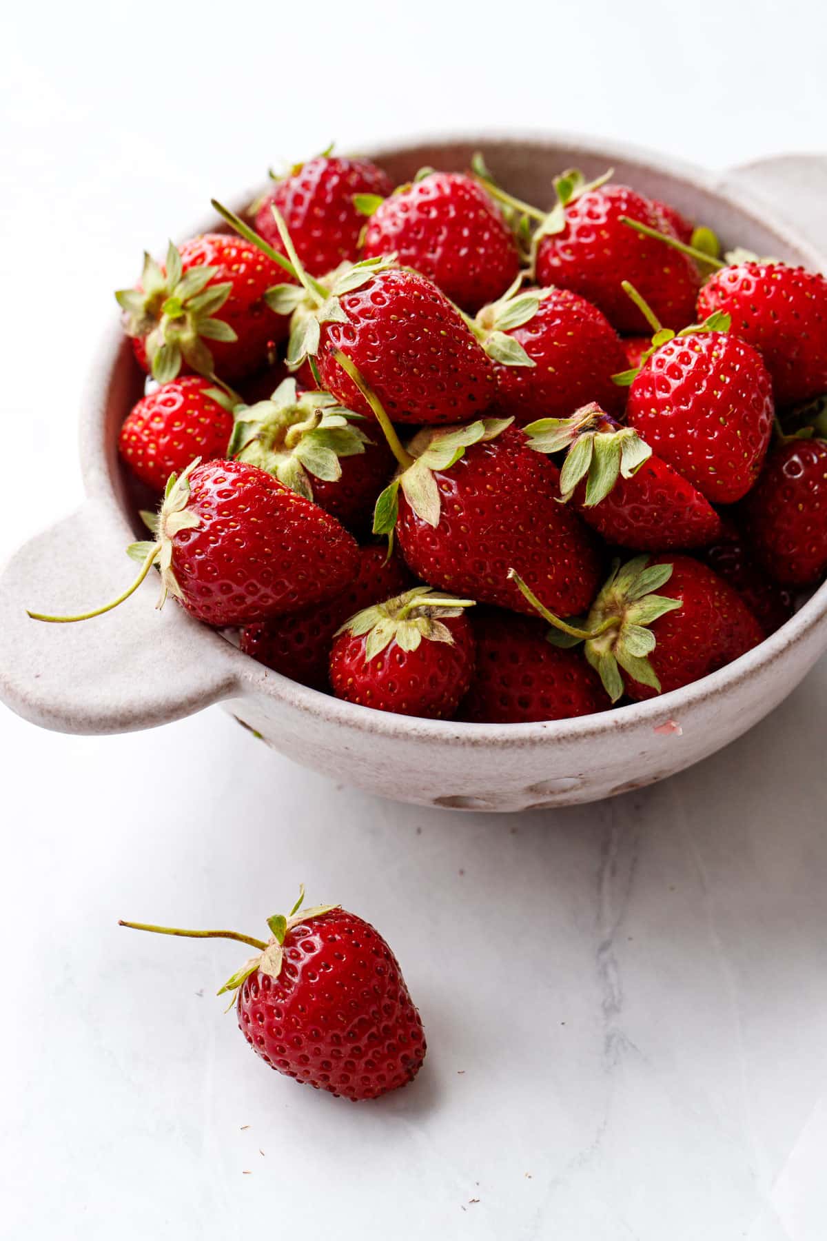 Ceramic berry bowl filled with fresh strawberries on a marble background.