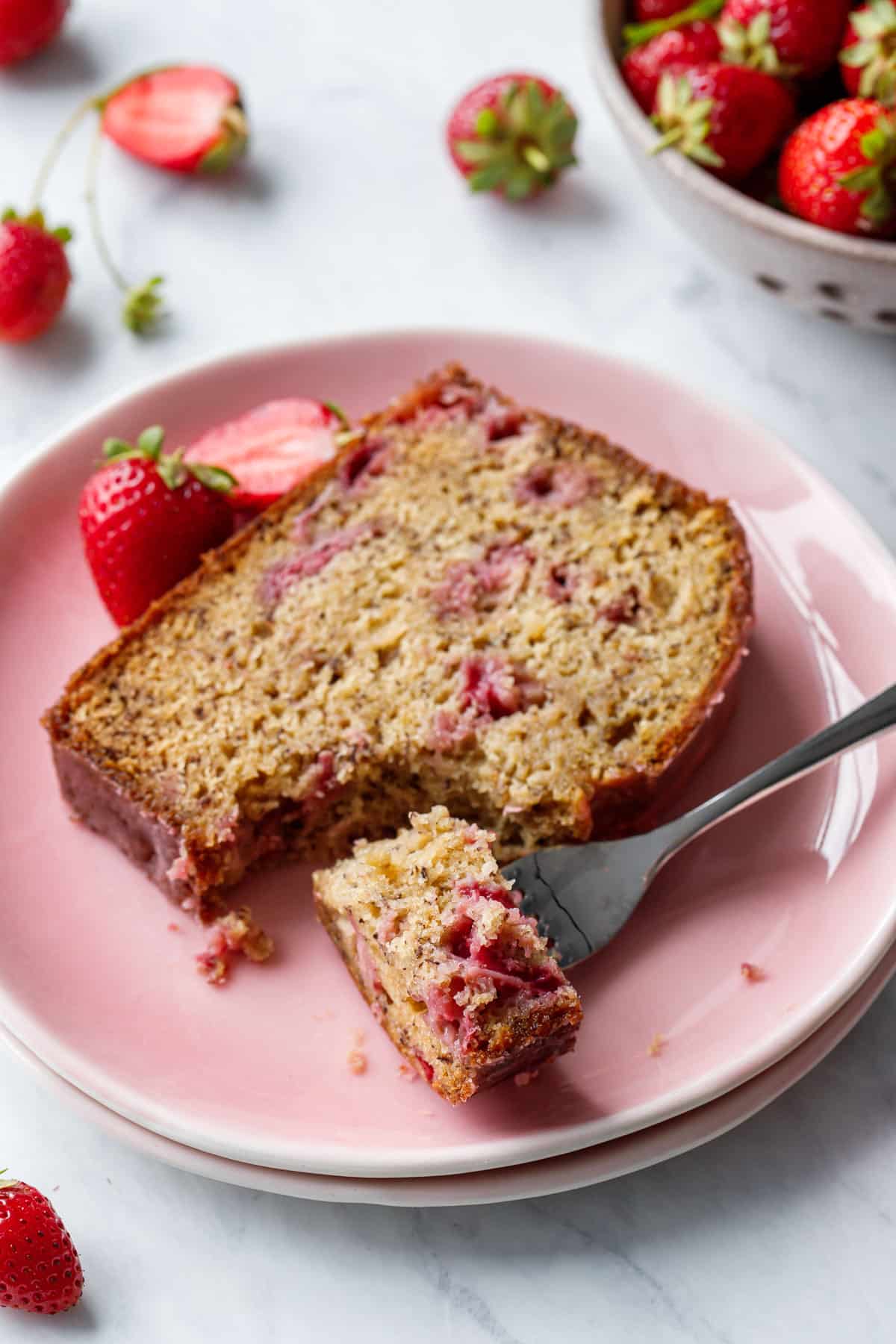 Slice of Strawberry Banana Bread on a pink plate, forkful cut out to show the moist texture.