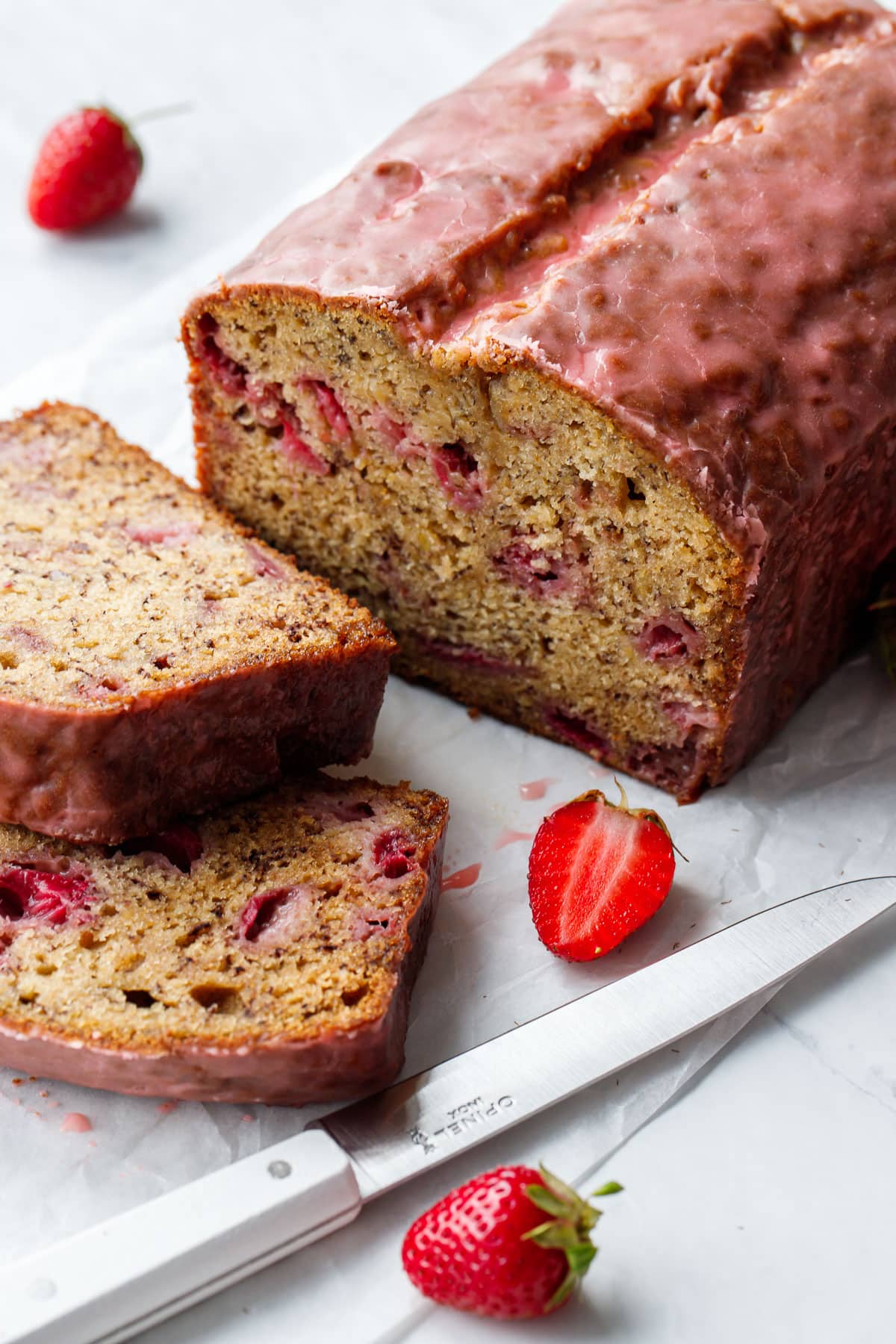 Sliced loaf of Strawberry Banana Bread covered with a pink strawberry glaze, cut section shows the moist texture and pieces of fresh strawberries scattered throughout.