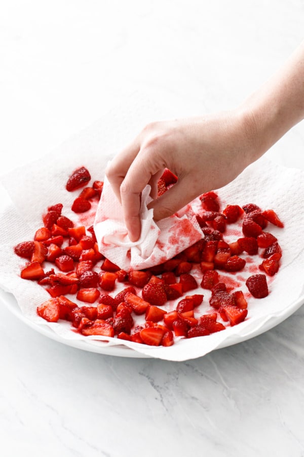 Patting the macerated strawberry pieces with a paper towel to dry them.