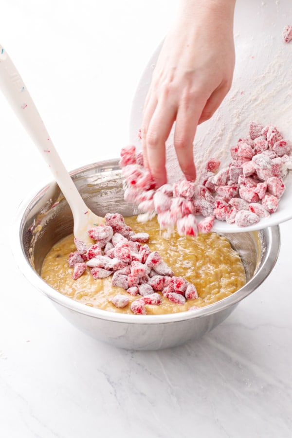 Adding the flour-coated strawberry pieces to the freshly mixed banana bread batter.