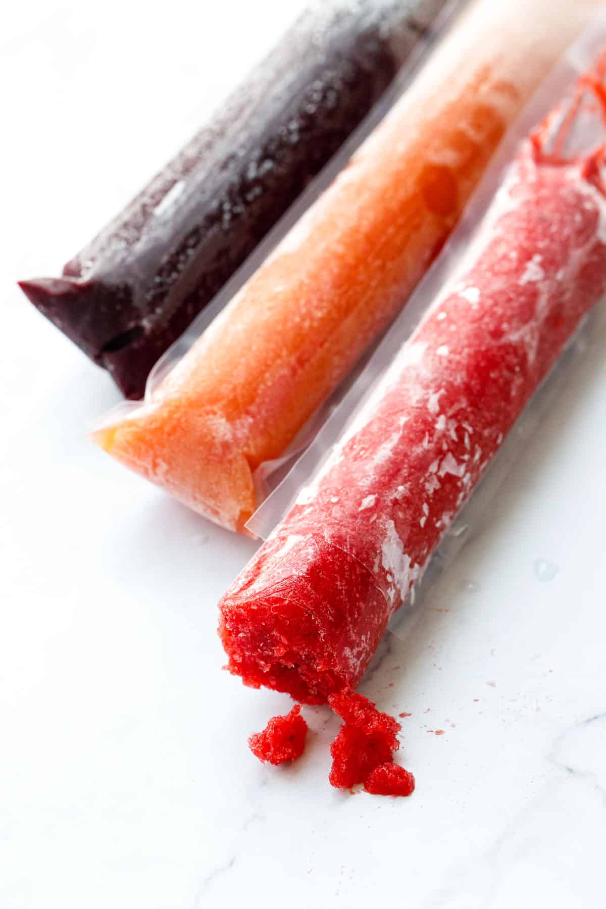 Three closeup Freezer Jam Fruit Ice Pops, one cut open and bitten into to show the unique texture.