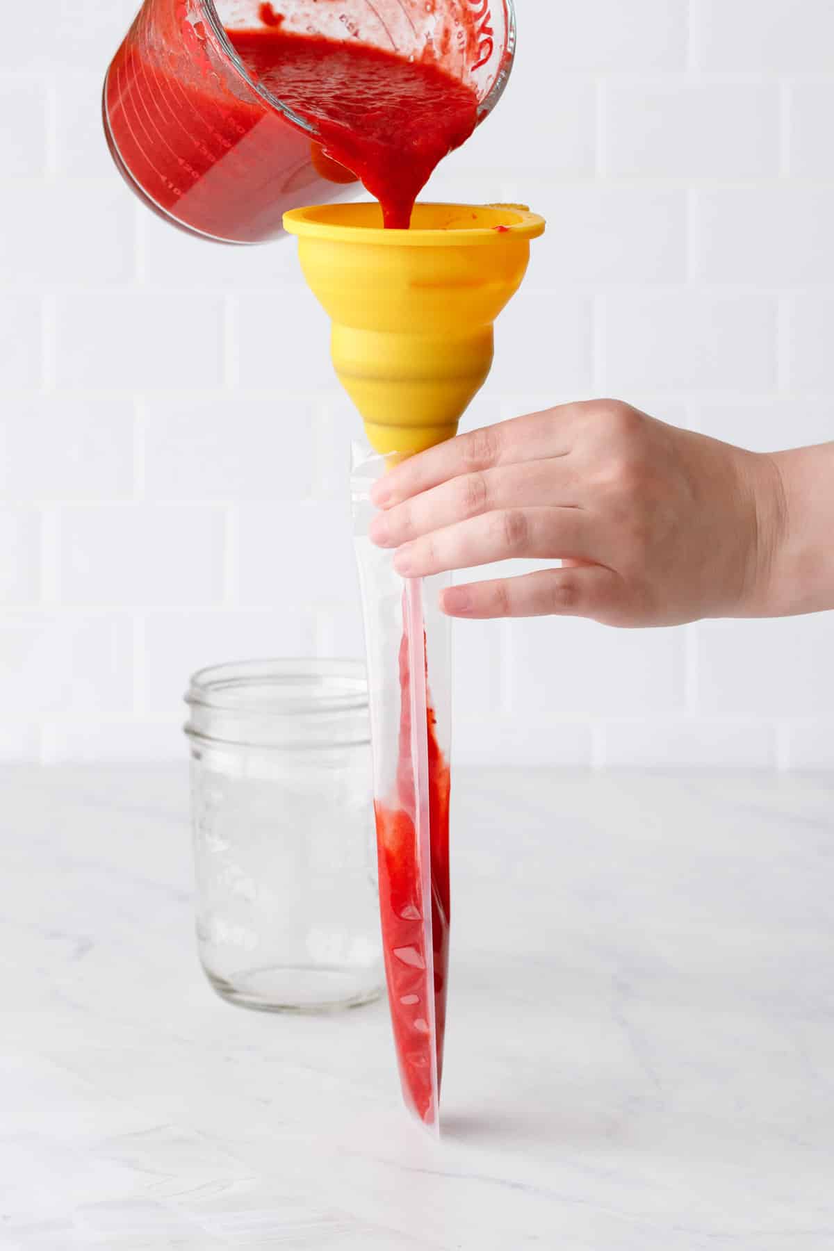 Filling the plastic ice pop pouch using a silicone funnel to fill with strawberry freezer jam.