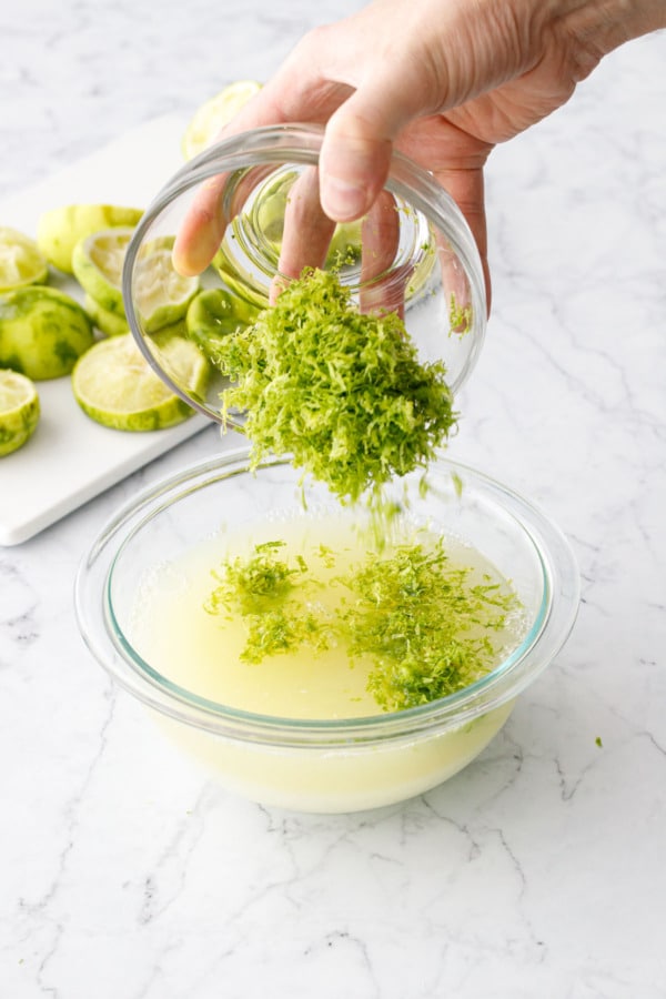 Pouring fresh lime zest into a bowl with lime juice and sugar.
