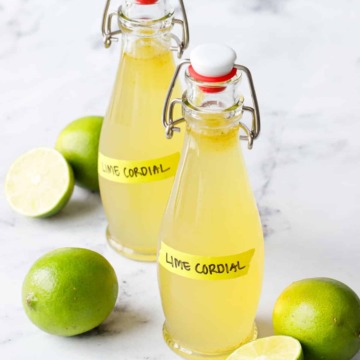 Two swingtop bottles filled with Homemade Lime Cordial on a marble background with fresh limes.