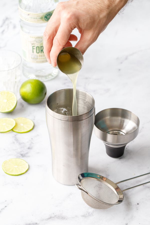 Pouring Homemade Lime Cordial into a cocktail shaker to make a Gimlet.