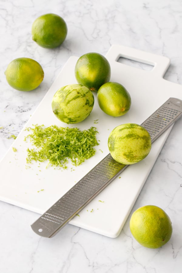 Zested limes with a microplane grater on a white cutting board.