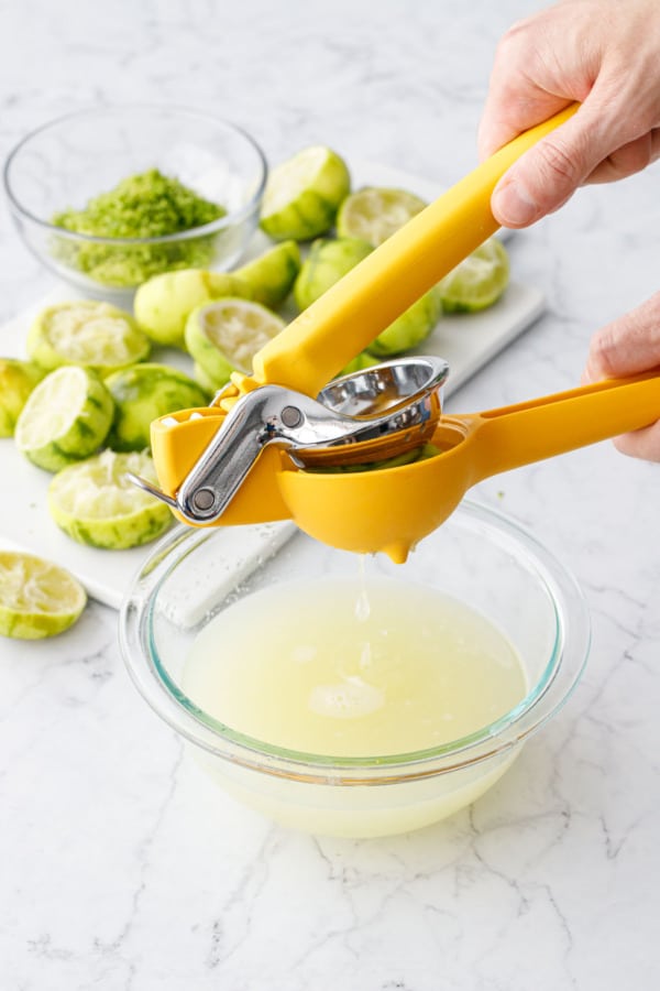 Citrus juicer squeezing limes into a bowl of juice, zested and juiced lime peels piled in the background.