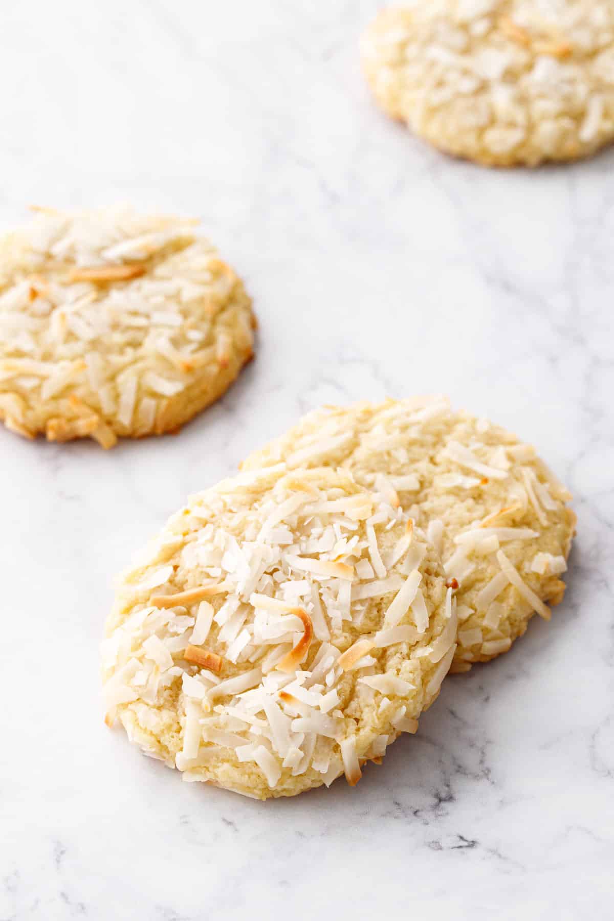 Toasted Coconut Sugar Cookies with visible coconut shreds on top, on a white marble background.