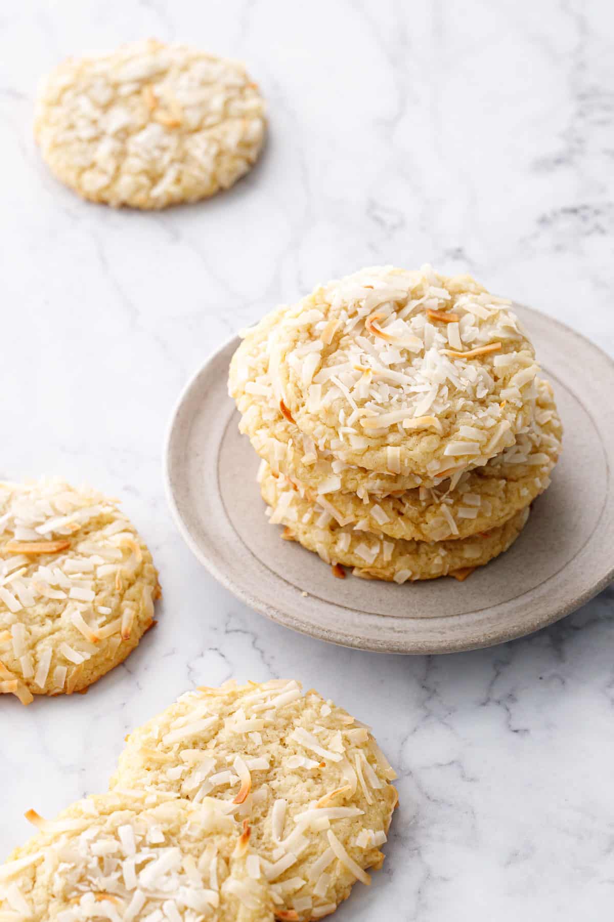 Stack of four Toasted Coconut Sugar Cookies on a gray plate, a few more cookies on the side on a marble background.