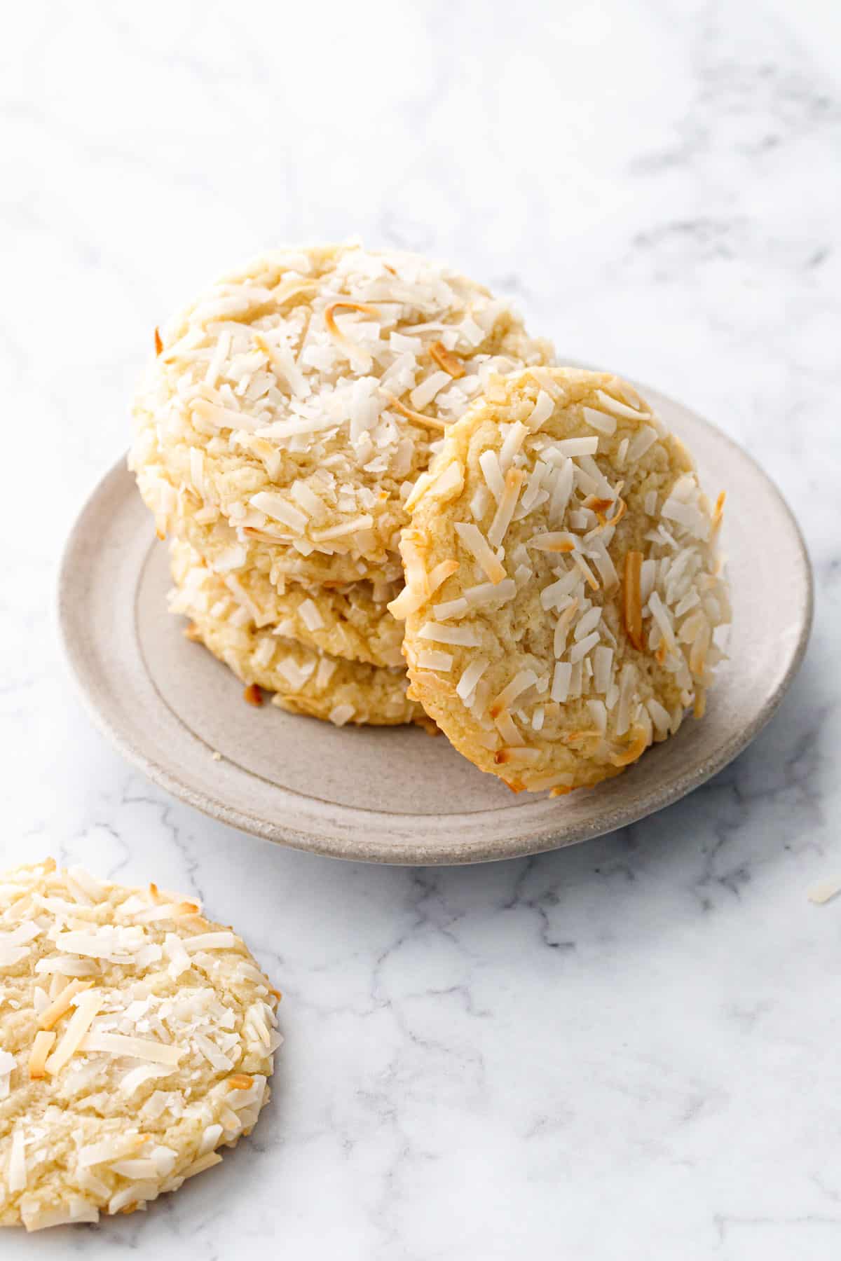Stack of Toasted Coconut Sugar Cookies on a plate with one cookie leaning up against the stack to show the toasted shredded coconut on top of the cookie.