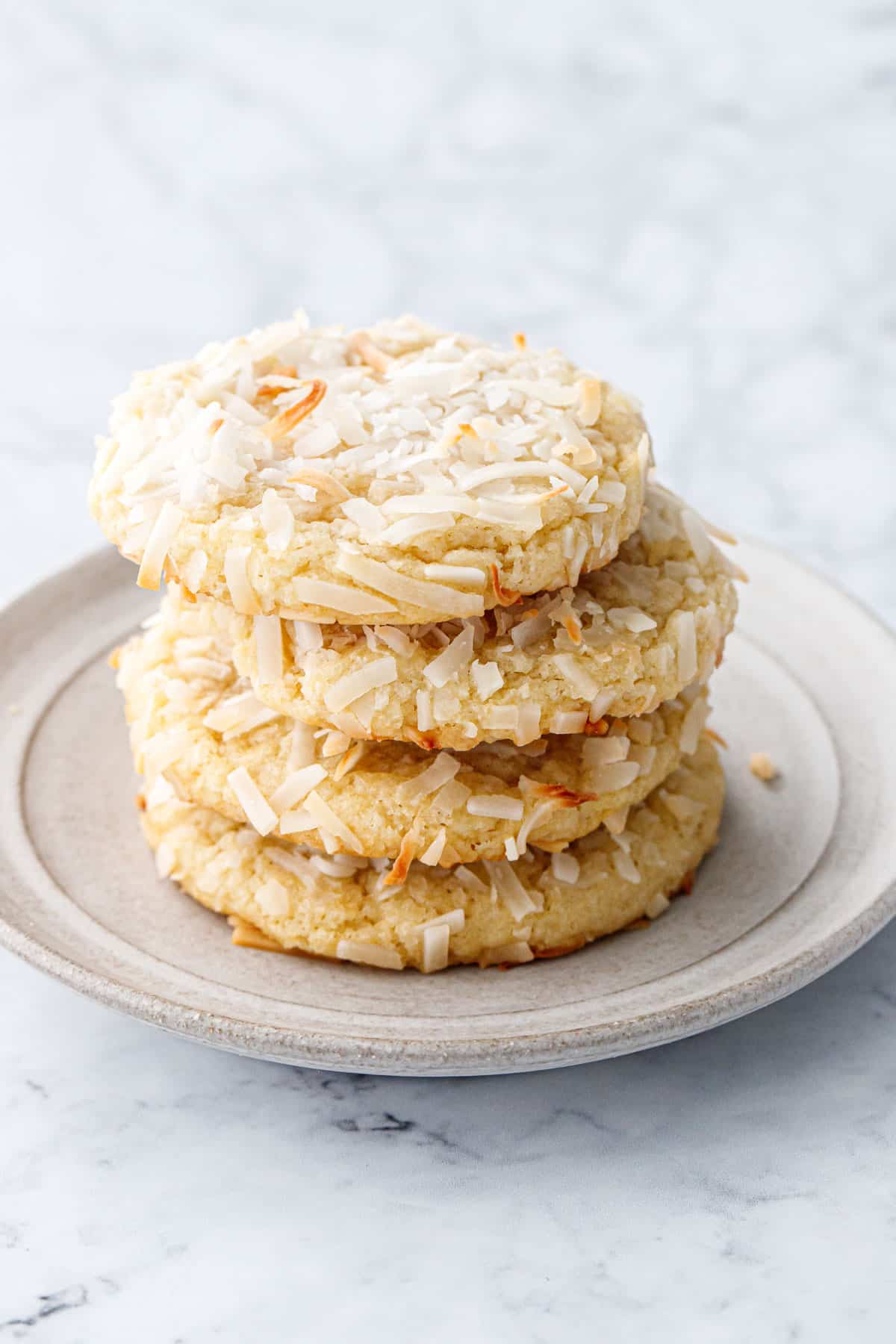 Stack of four Toasted Coconut Sugar Cookies on a ceramic plate sitting on a marble background.