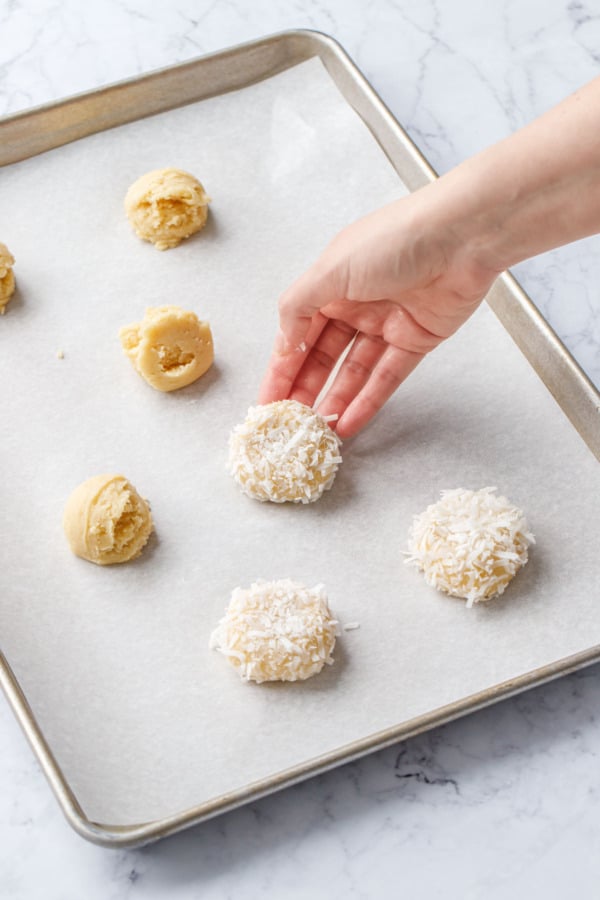 Placing coconut-covered dough ball onto a parchment-lined baking sheet.