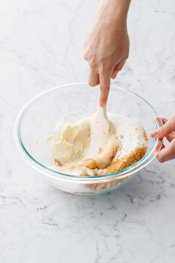 Spatula mixing together ingredients in a glass mixing bowl.