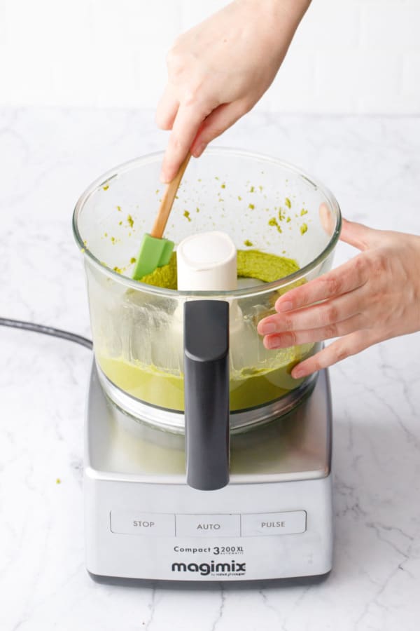 Scraping down the side of the food processor with a green spatula to ensure even mixing.