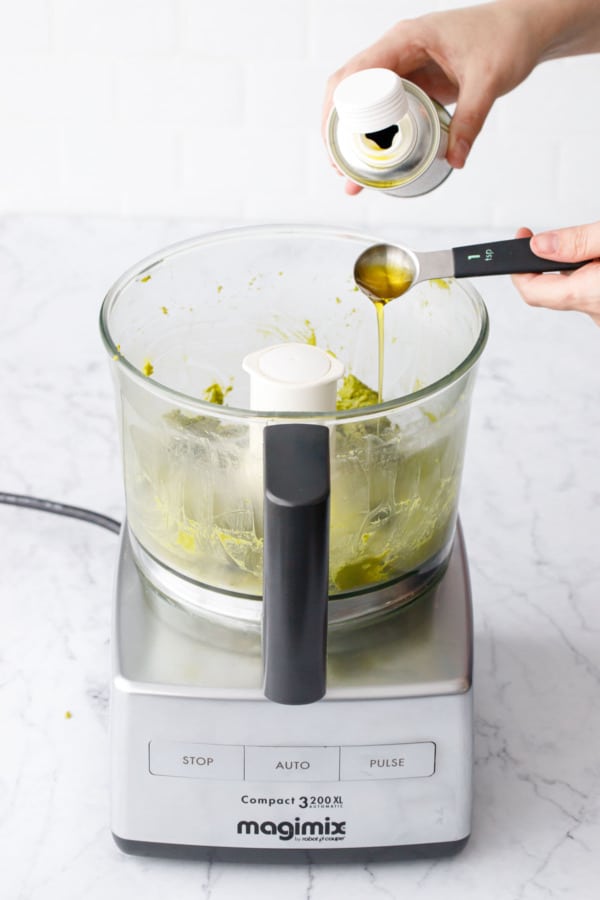 Pouring in 1 teaspoon of toasted pistachio oil to smooth out the Homemade Pistachio Butter.