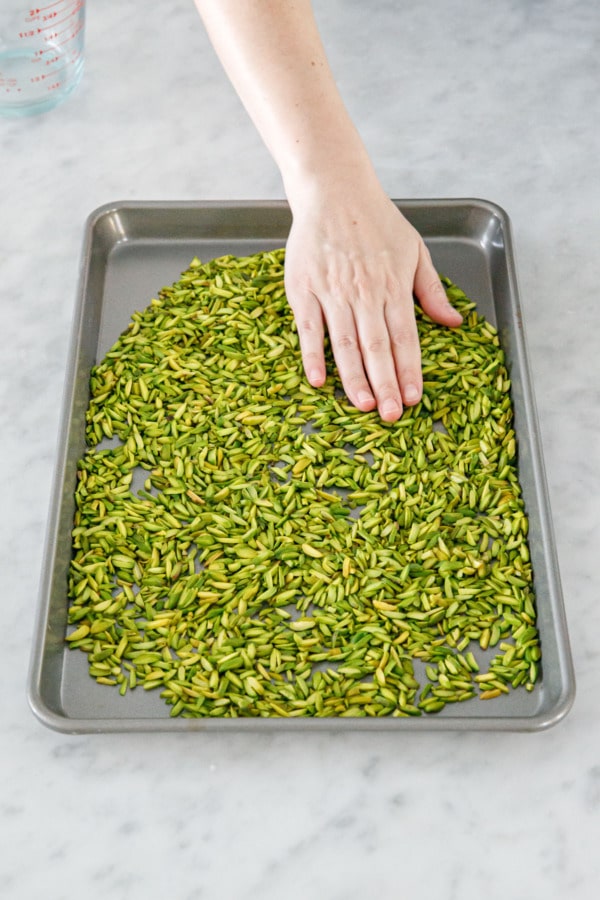 Spreading slivered pistachios onto a baking sheet to lightly toast them in the oven.