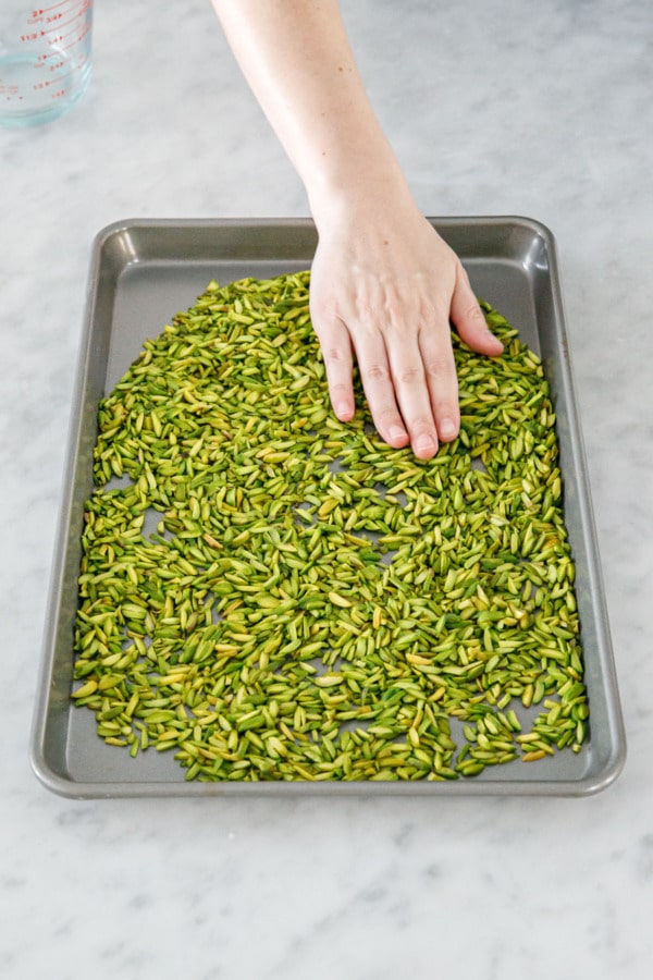 Spreading slivered pistachios onto a baking sheet to lightly toast them in the oven.